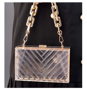 Detail view of clear acrylic clutch with V-pattern texture and pearl gold chain strap