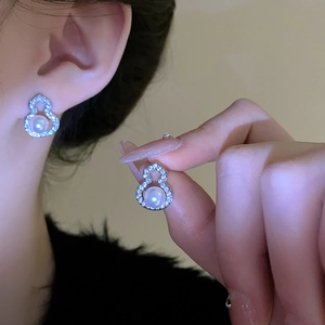 Detailed view of silver gourd earrings with zircon inlay and white pearl drops on ear