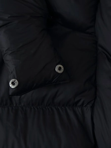 Macro shot of silver metal snap buttons on black padded coat sleeve and smooth fabric