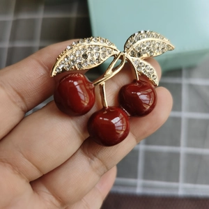 Gros plan d'une broche cerise rouge avec feuilles dorées et strass brillants