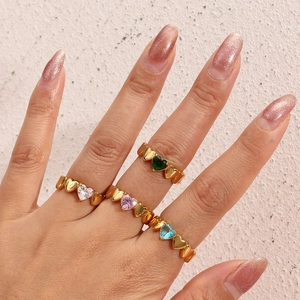 Close-up of four gold heart-shaped rings set with clear, pink, blue, and green crystals