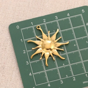 Detailed top view of a gold sunflower pendant with dimensions shown on a green scale mat