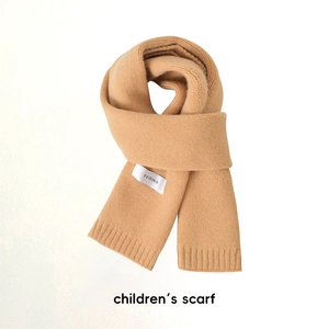 Détail d'une écharpe en tricot beige pour enfant avec étiquette de marque sur fond blanc