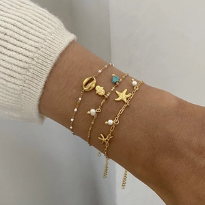 Three-piece gold sea shell and pearl charm bracelets set worn on a female wrist