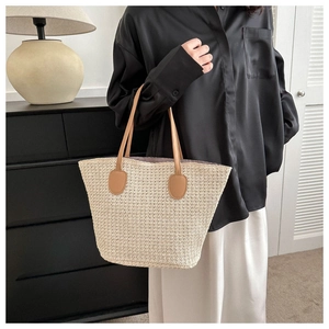Close-up of beige straw woven tote bag with camel leather handle on elegant female model