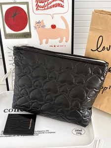 Detail of black quilted heart makeup bag with elegant pearl carrying chain on tray