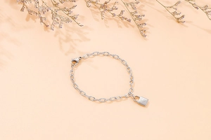 Close-up of silver chain bracelet with padlock pendant over a soft beige background
