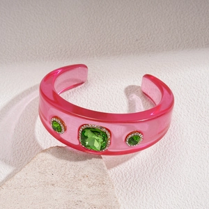 Close-up of pink resin bangle featuring green gemstones and sparkling micro-pave crystals
