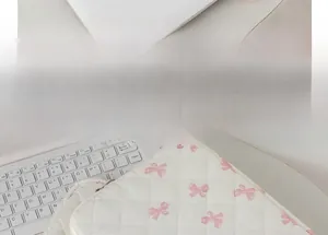 Close-up of quilted white tablet sleeve with pink bow pattern next to a laptop