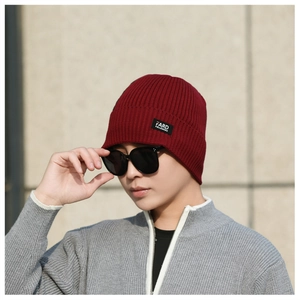 Detailed view of dark red ribbed knit beanie featuring a black square brand logo patch