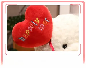 Close-up of a white teddy bear holding a red heart pillow with happily met embroidery