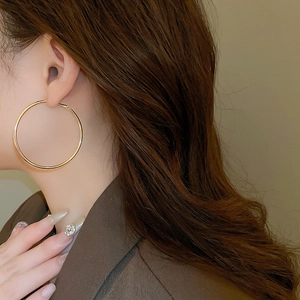 Close-up of a large golden hoop earring worn by a model to show texture and shine
