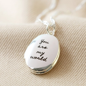 Detail of silver oval locket necklace with You are my world engraving on soft fabric