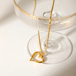 Golden stainless steel heart pendant necklace draped over an elegant glass goblet