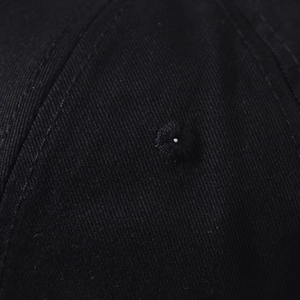 Close-up of black denim twill fabric and top button detailing on the baseball cap
