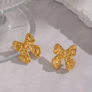 Macro detail of golden metal bow stud earrings with a unique pleated texture finish