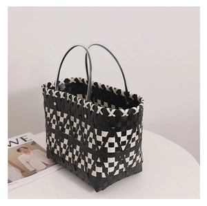 Detail of hand-woven black and white checkered straw tote bag with clear round handles