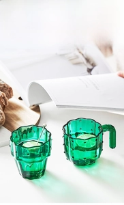 Close-up of green cactus-textured glass cups and a metal stir stick on a wooden tray
