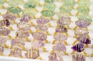 Close-up of handmade amethyst and fluorite raw stone rings in a white jewelry display box