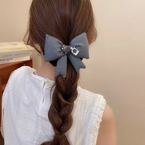 Dettaglio dello scrunchie grigio a fiocco con cristallo e ciondolo a boccetta di profumo