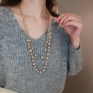 Detail of layered gold metal chain with champagne pearls on a grey knit sweater