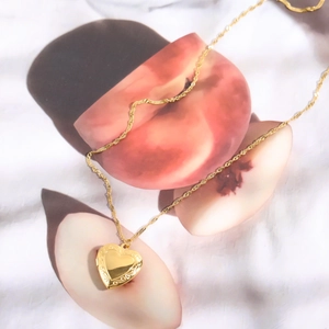 Golden stainless steel heart locket necklace with embossed patterns on peach background