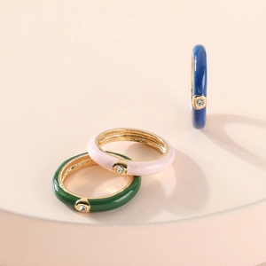 Detailed view of three enamel rings in pink, green and blue with zircon on a beige stand