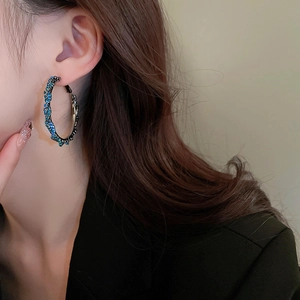 Macro shot of a model wearing large silver-tone hoop earrings with blue rhinestones