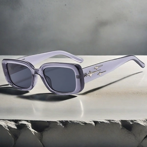 Detail of transparent purple square sunglasses with silver star accents on marble surface