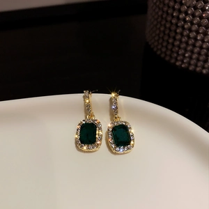 Macro shot of elegant gold earrings with emerald green stone and sparkling diamond halo