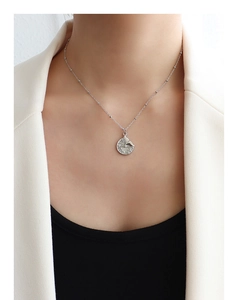 Close-up of silver necklace featuring a round fish tail pendant on a thin bead chain
