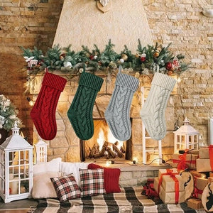 Quattro calze di Natale in maglia con motivi a trecce appese a un caminetto decorato a festa