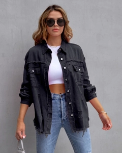 Detail einer schwarzen Jeansjacke mit Fransenrand und Metallknöpfen am Model getragen