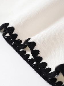 Detailaufnahme der weißen Strickweste mit schwarzer Kontrastkante und feiner Textur