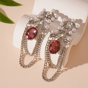 Detailed close-up of vintage earrings with ruby red stones and faux pearls on white stone