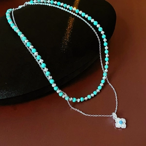 Detail of beaded turquoise necklace with a silver four-leaf clover pendant on a black stand
