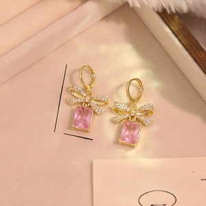Dettaglio di orecchini a fiocco dorati con zircone rosa e misure del prodotto