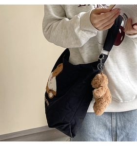 Close-up of black quilted tote bag with teddy bear embroidery and plush charm
