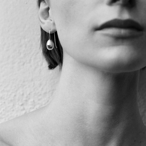 Artistic black and white close-up of a minimalist silver teardrop earring on a model