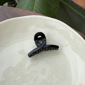 Detail view of the black glossy hair clip on a beige plate with leaf background