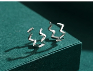 Macro shot of polished silver wave ear cuffs on a minimalist dark green geometric stand