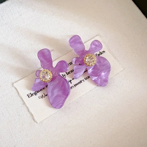 Détail de boucles d'oreilles fleur en résine violette avec serti doré et zircon central