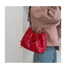 Detail of red pleated PU leather shoulder bag with large bow decorations and chain strap