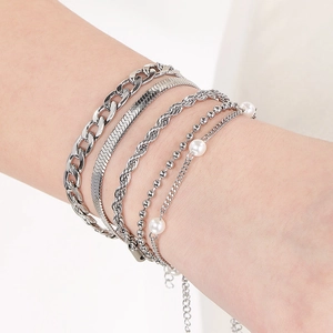 Close-up of stacked silver bracelets including snake, rope, and pearl bead chains on wrist