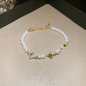 Elegant gold bracelet with green emerald-cut stones and white pearls on a textured background