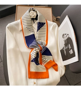 Polka dot and geometric silk scarf knotted on white shirt collar shown in close-up detail