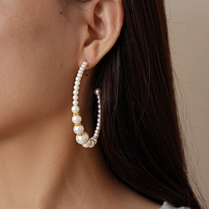 Detailed close-up of large C-shaped hoop earrings with white pearls and gold spacers