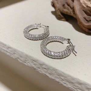 Dettaglio di orecchini a cerchio argentati con micro-pavé di zirconi bianchi lucidi
