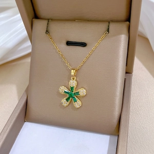 Elegant gold titanium flower necklace with green gemstones and white crystals in a jewelry box