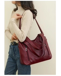 Detail of wine red faux leather shoulder bag with multiple zippers and silver hardware